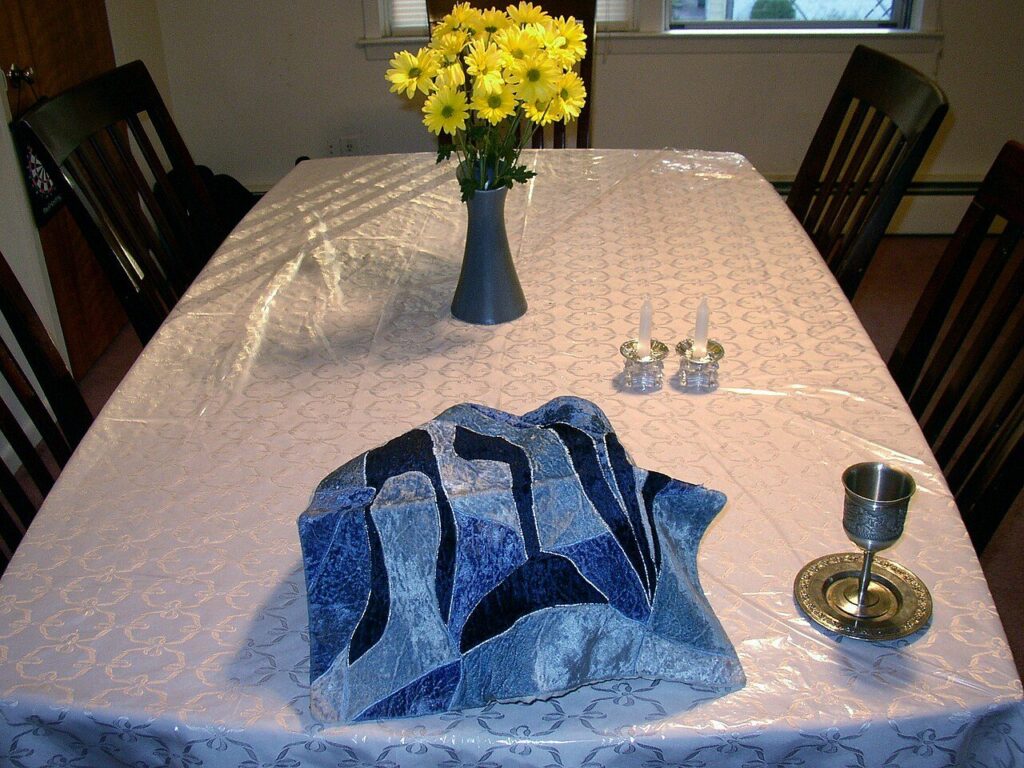 Kosher for Shabbat table setting with covered challah, a kiddush cup, and candles
